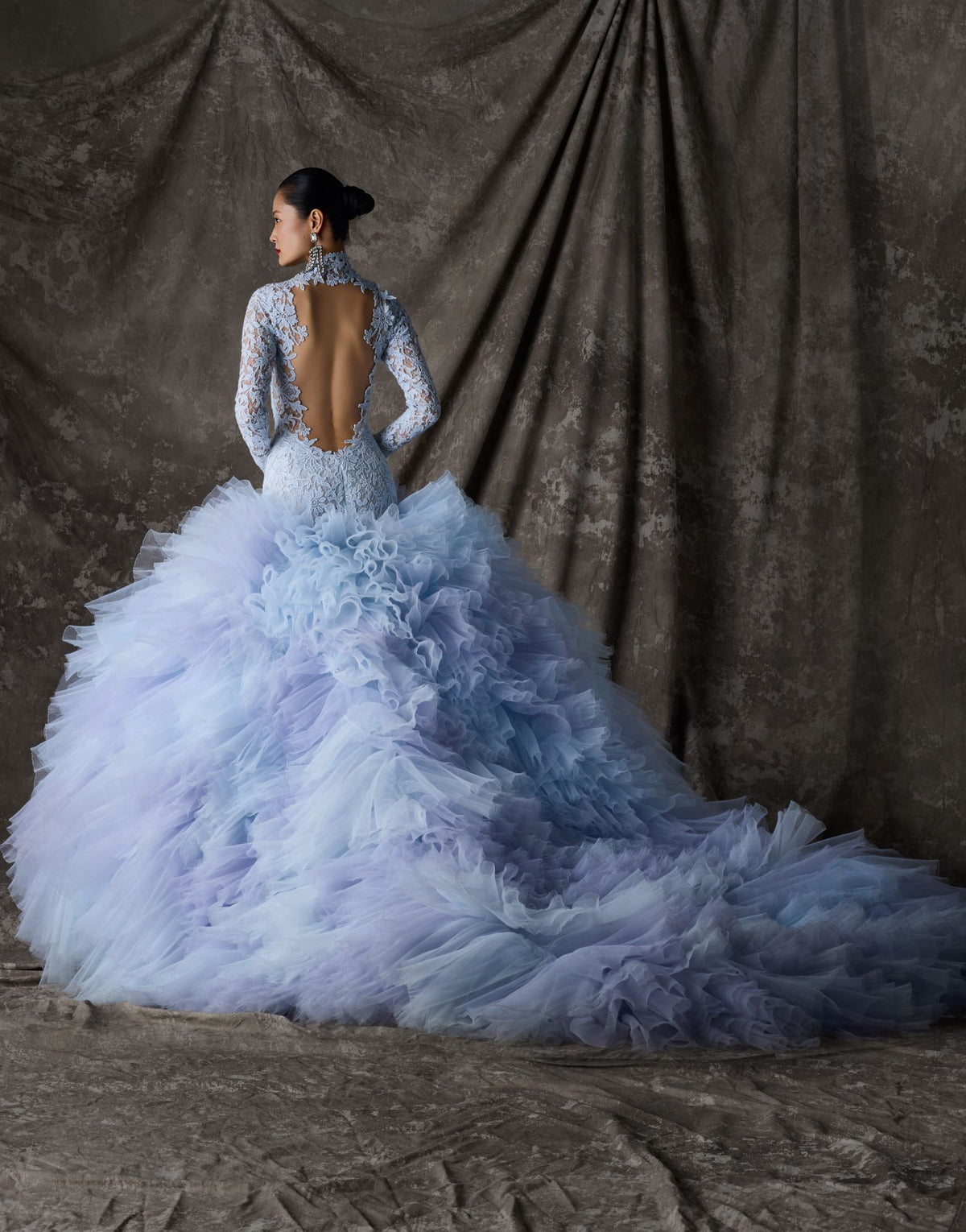 Blue lace and tulle ballgown with open back and long train against a textured brown backdrop