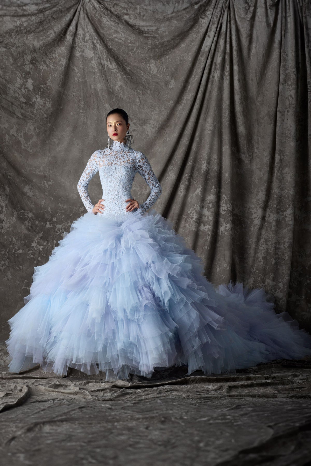 Woman in a light blue lace and tulle ballgown against a textured gray curtain